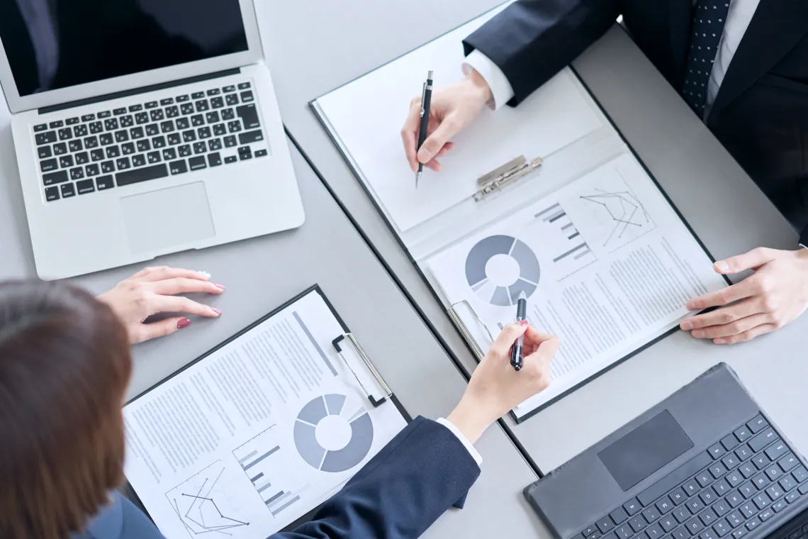 ノートパソコンと資料を囲んで打ち合わせをするビジネスチームの様子