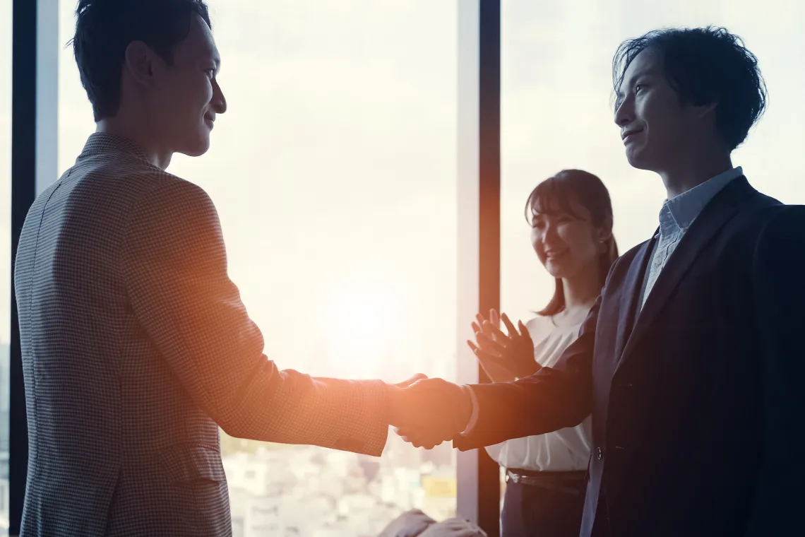 夕日を背景に握手を交わすビジネスパーソンのシルエット